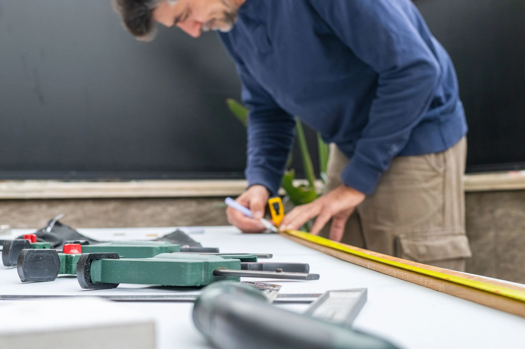 Person measuring timber with tape measure on workbench